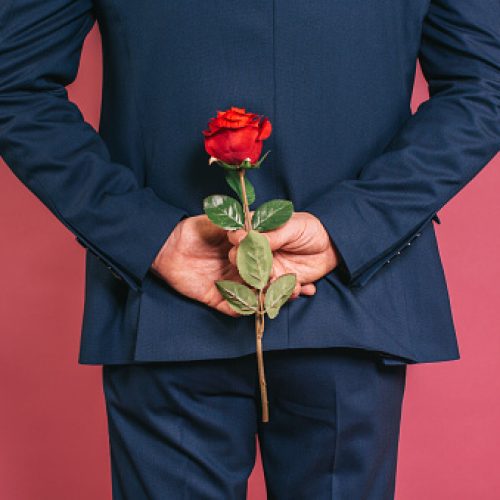 Unrecognizable charming well dressed man holding a red rose